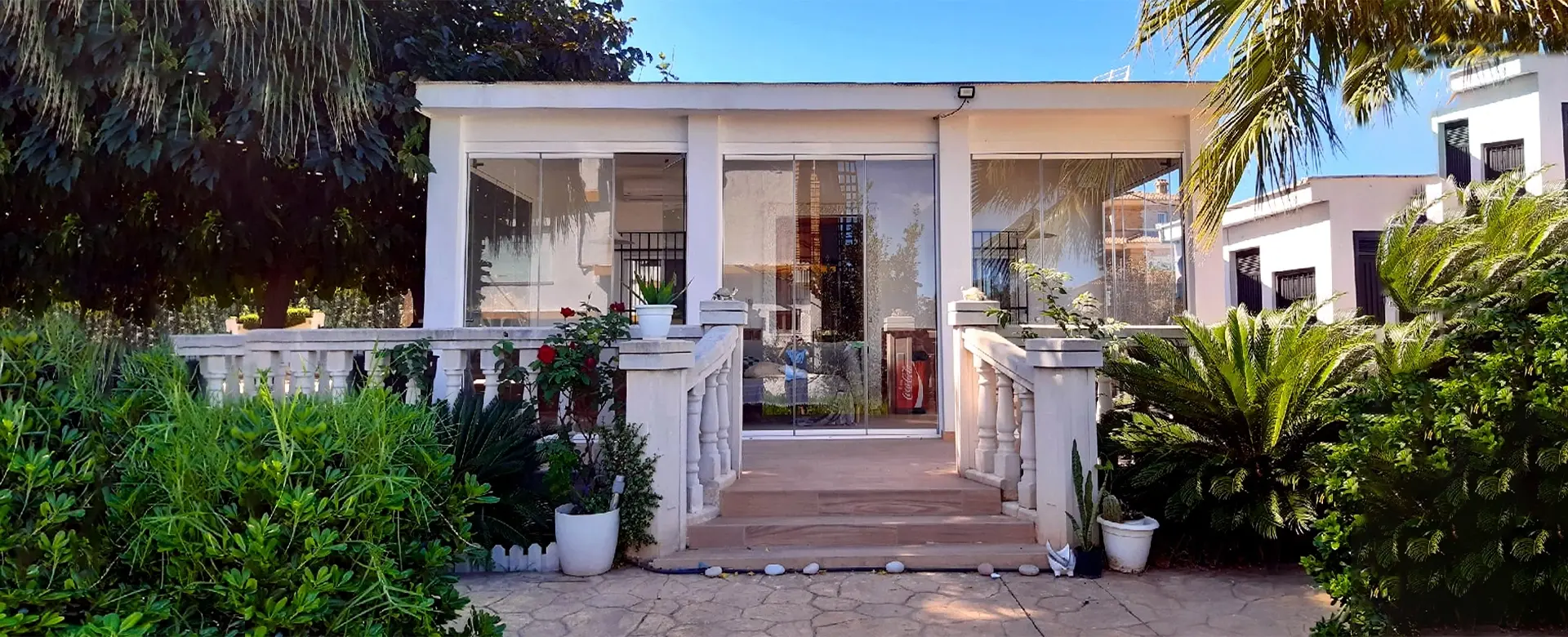 Una veranda con acristalamiento panorámico, rodeada de vegetación y plantas decorativas.